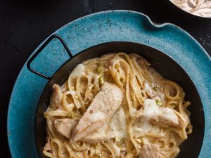 top view chicken fettuccine alfredo on blue plate with cheese aside