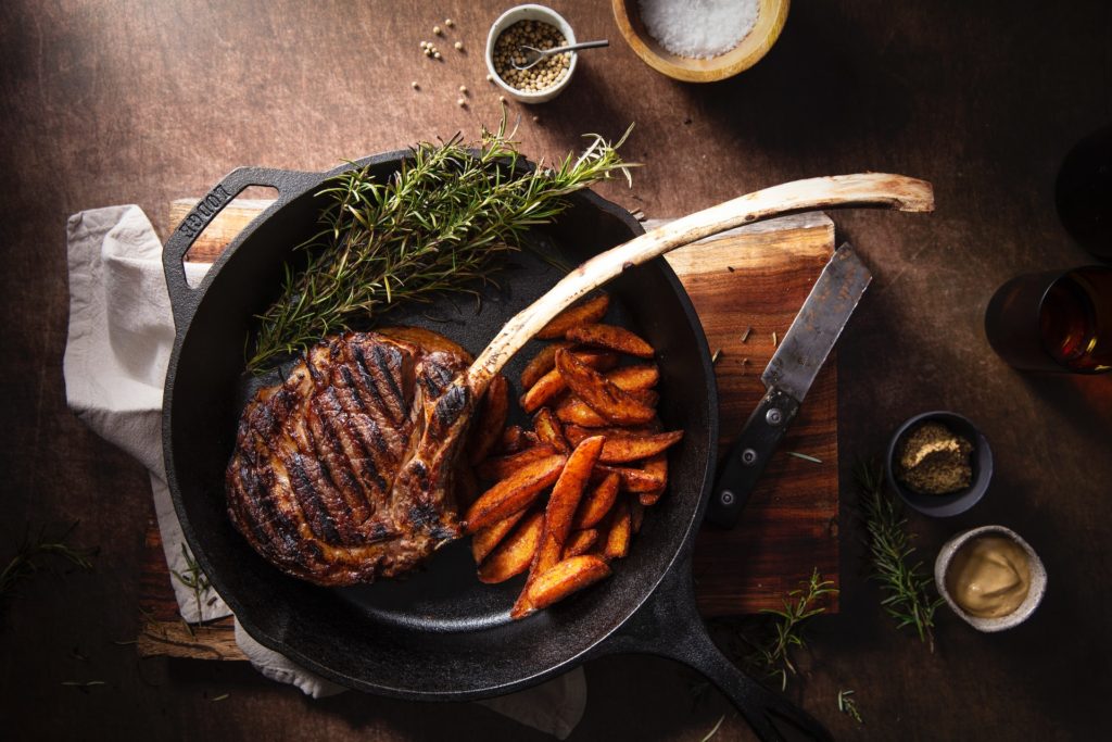 grilled tomahawk steak medium well with fried potato on cast iron pan