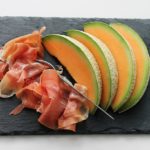 Sliced Parma Ham and melon on a black plate