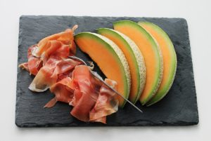 Sliced Parma Ham and melon on a black plate