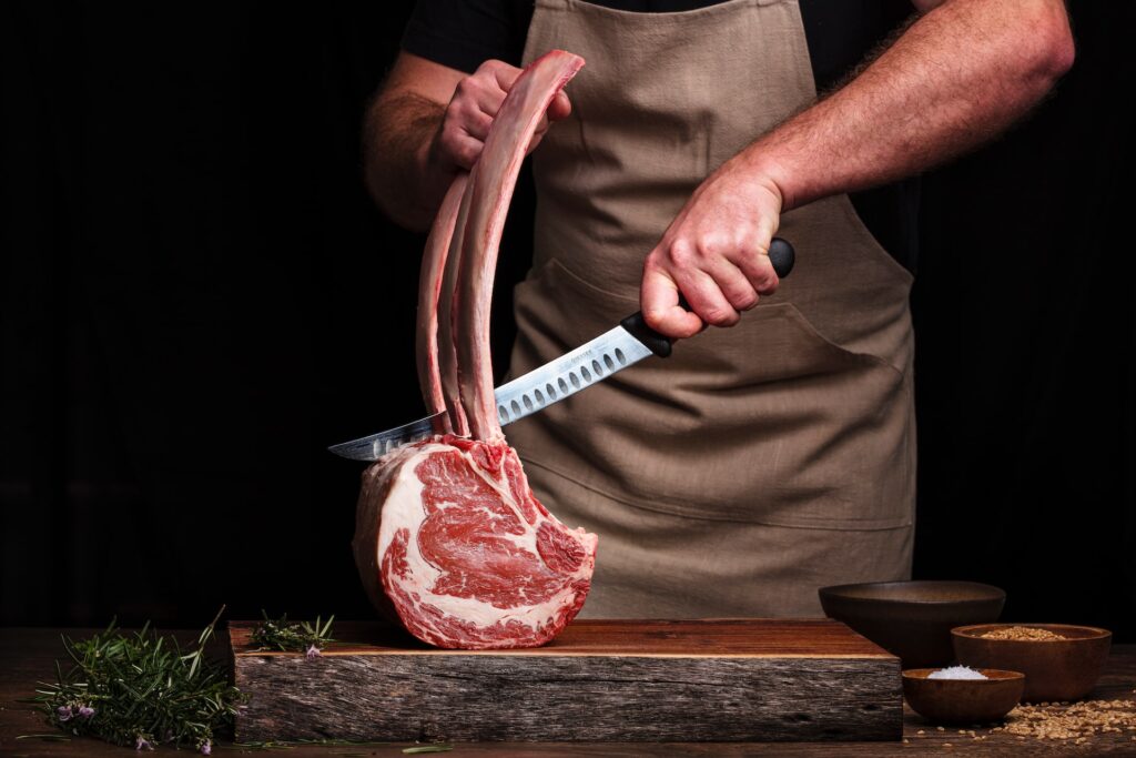 A butcher is holding a large rib bone and butchering a Tomahawk Ribeye Steak