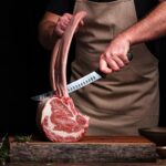 A butcher is holding a large rib bone and butchering a Tomahawk Ribeye Steak