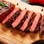 Grilled sliced steak topped with herbs on wooden board