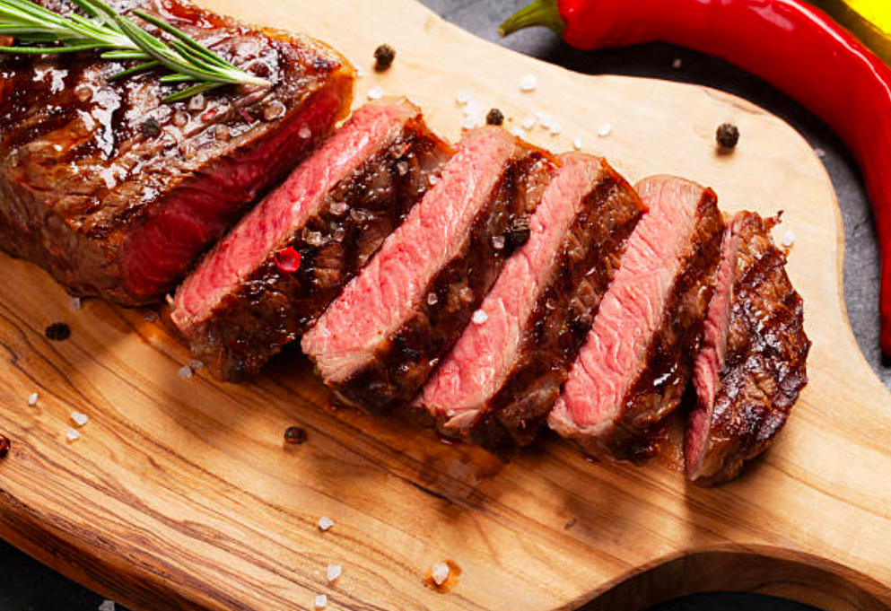 Grilled sliced steak topped with herbs on wooden board
